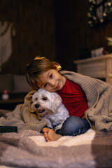 Little toddler child, boy, lying in bed with pet dog, little maltese dog, reading a book.