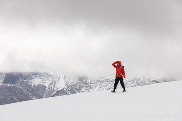 Fototapeta na wymiar A man in an orange jacket stands on a snowy mountain peak, looking out at the landscape. The scene is serene and peaceful, with the man's gaze focused on the horizon