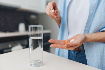 Close up of woman holding orange pill in front of glass of water and pill bottle on table