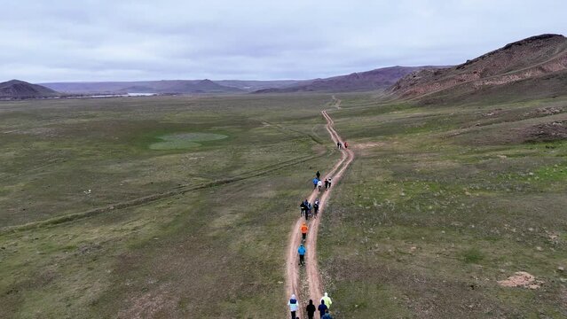 Outdoor competition, trail running. A large group of athletes running on a dirt road in a river valley on an early overcast morning. Drone footage