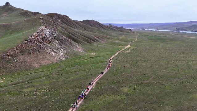 Outdoor competition, trail running. A large group of athletes running on a dirt road in a river valley on an early overcast morning. Drone footage