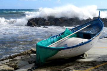 Boat rests on the shore near a rocky ledge as waves crash in the distance