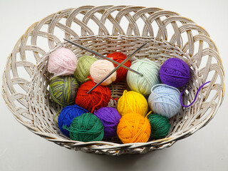 Colorful balls of wool for knitting and knitting needles lie in a white wicker basket