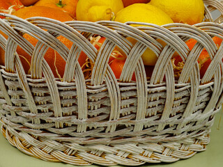 Fresh tangerines and grapefruits lie in the white wicker basket  on the green table,  a delicious gift