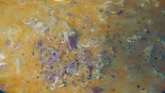 Full frame close-up: Black pepper is added to simmering meaty stew