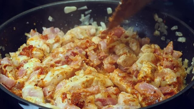 Chicken curry simmers, bubbles in pan, stirred with wooden spatula