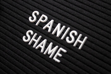The word spanish shame on black letter board over isolated beige background. Psychological concept