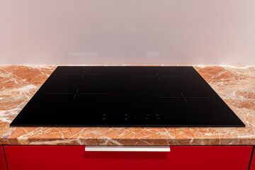 Sleek modern induction cooktop on a marble counter against a red backdrop