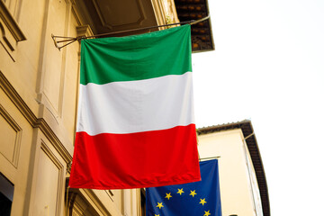 Flag of Italy with EU flag hanging on the wall of a house. Flags in the facade of old building - obrazy, fototapety, plakaty