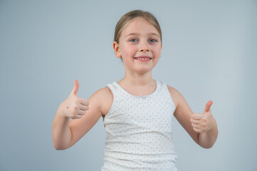 Caucasian 6 year old girl showing thumbs up against white background. 