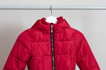 Red child puffer coat hanging over white background © Tatiana Foxy