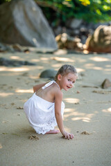 Little girl in white dress having fun on seashore in the shade of trees and palms.