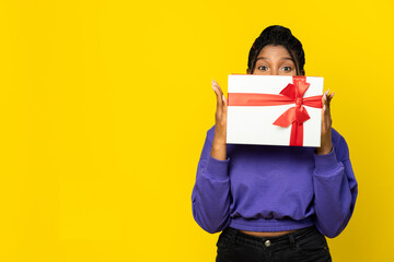 Woman holding a white gift box with a vibrant red ribbon against a yellow background.