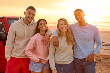 Portrait Of Couple With Friends Standing By Car At Beach Watching Sunrise Together