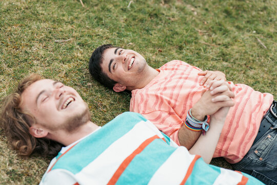 Two men, deeply in love and both transgender, enjoy each other's company, smiling and holding hands on a grassy field
