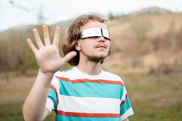 A man in mirrored sunglasses makes a stop gesture, evoking a sense of boundary or awareness in an outdoor setting