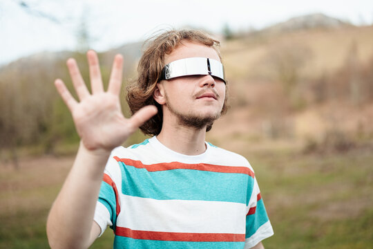A man in mirrored sunglasses makes a stop gesture, evoking a sense of boundary or awareness in an outdoor setting