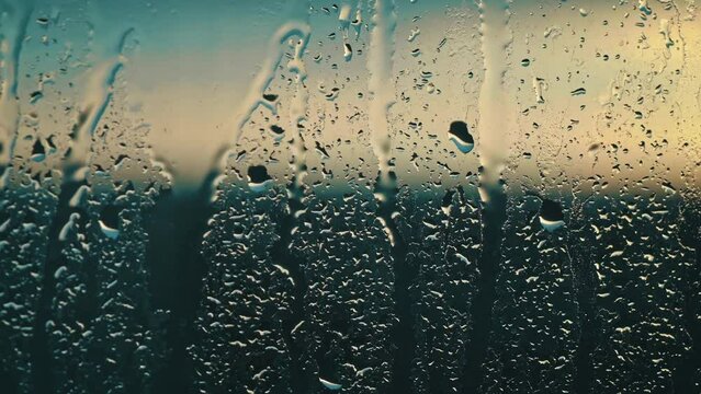 Evening rain plays a melancholic serenade on the glass, with droplets illuminated by a dusky glow