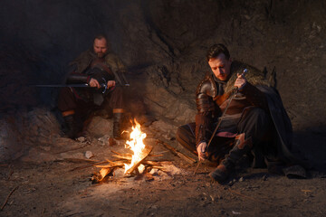 Medieval knights sharpen swords by fire in cave - 773976761