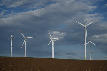 Six wind turbines of different types in the evening sun under a partly cloudy sky. Near Giessen in...