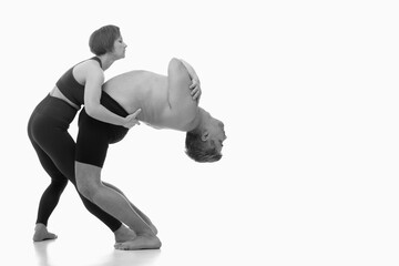 Work with an instructor, Ashtanga yoga  Side view of man and woman doing Yoga exercise against white background. Black and white image. Copy space for text or design.