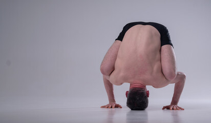 Urdhva Kukkutasana (variation), Ashtanga yoga  Side view of man wearing sportswear doing Yoga exercise against gray background. Copy space for text or design.