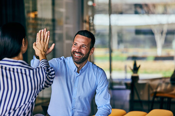 A smiling businessman gives a high-five to his female assistant.