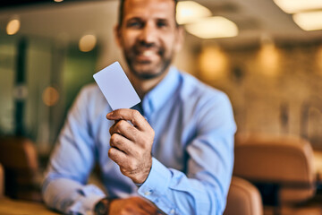 A smiling businessman holding a credit card, working at the office.
