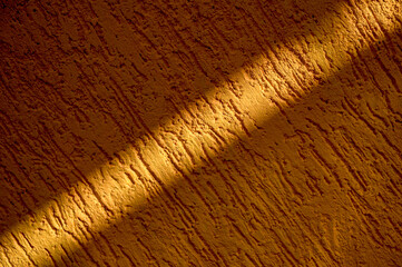 The orange textured cement wall has sunlight streaking diagonally in the morning.