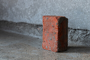 Brick made of soil placed vertically on concrete floor at construction of home with cement plastered wall background.