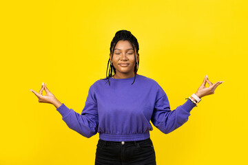 Young woman meditating in purple sweater with closed eyes and zen fingers isolated over yellow background.