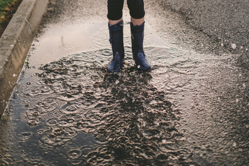 a girl jumping into a puddle in purple rain boots