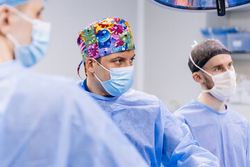 Experienced surgeons in medical gowns, caps, masks and gloves perform an operation in a modern...