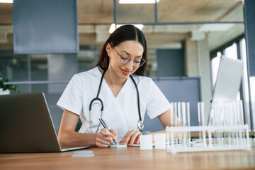 Writing by the using a pen. Female doctor in white coat is indoors
