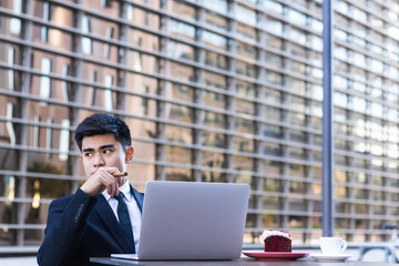 Young Asian office worker having a breakfast while working on laptop