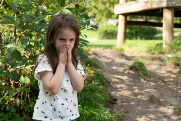 Little girl covering her mouth with her hands in the park on a sunny day