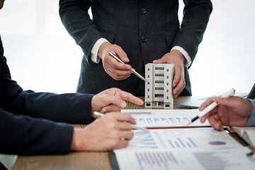 A professional businessman in a suit conducts a meeting at a desk while showcasing a model of a...