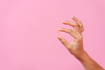 Gracefully, woman hand cradles a bottle of cod liver oil against a pink backdrop, representing health, nutrition, and the benefits of omega-3 supplementation.