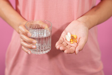 A professional image showcasing a female hand delicately holding a bottle of cod liver oil with her fingers against a soft pink isolated background.