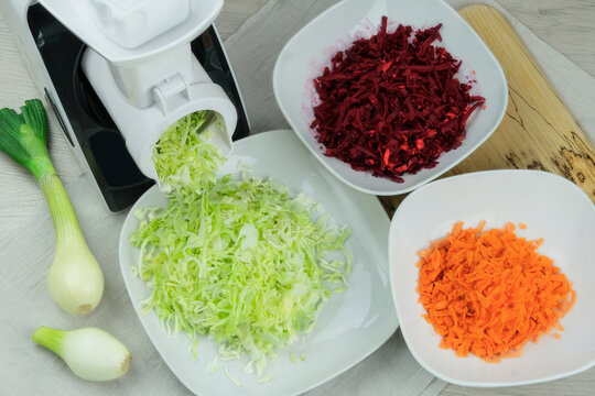 Cabbage, carrot, beets and onion in a vegetable cutter on kitchen table. Chopped carrot is falling into a bowl. Homemade healthy food. Health line.