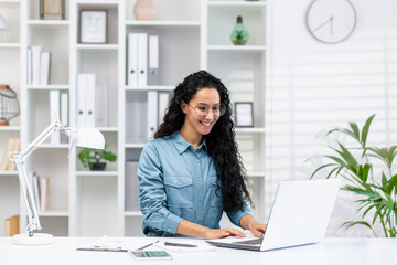 Smiling Hispanic woman focused on work at her home office, exuding professionalism and confidence...