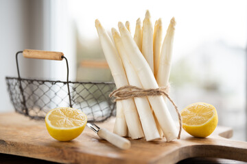 Standing bunch of fresh white asparagus. Seasonal spring vegetables with lemon on wooden cutting board. Kitchen scene for the seasonal gastronomy.