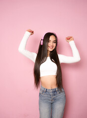 Young happy fun latin woman wear casual clothes and headphones listen to music dance gesticulating hands isolated on pink background studio portrait. Lifestyle concept