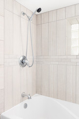 A bathroom shower with light brown or tan tiles with a chrome faucet and showerhead over a white...