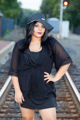 An overweight fashionable Indian woman from South Asia stands on the train tracks