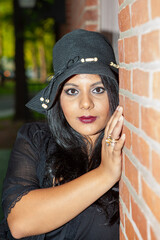 Southern Asian Indian woman in a black dress is wearing a black hat and a gold rings