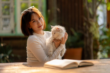 A woman shares a tender moment with her fluffy cat during a break from reading a book in a cozy...