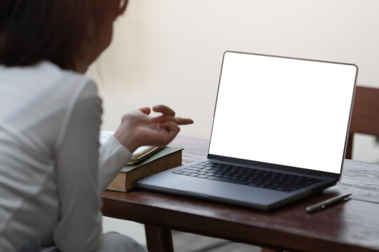 Over-the-shoulder view of a person using a laptop with a blank screen, ideal for web design mockups, at a wooden table.