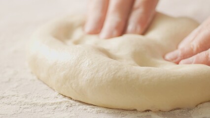 A moment of pizza creation, with fingers pressing into the soft dough to form the raised edge of...