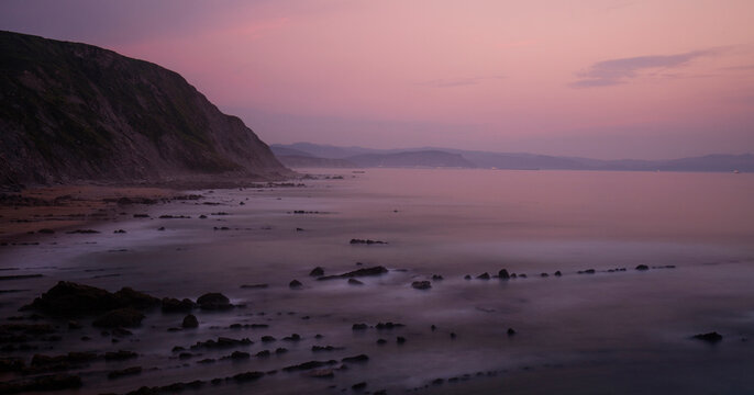 The sun's last light paints the skies and sea in shades of pink and purple at Playa de Barrika in Bilbao, with rocks ghostly in the surf